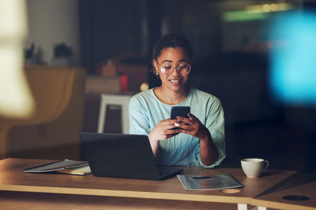 A woman checks her phone and laptop at her office.