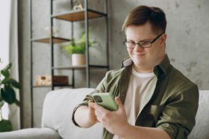 A happy Downs Syndrome young man uses a mobile phone.